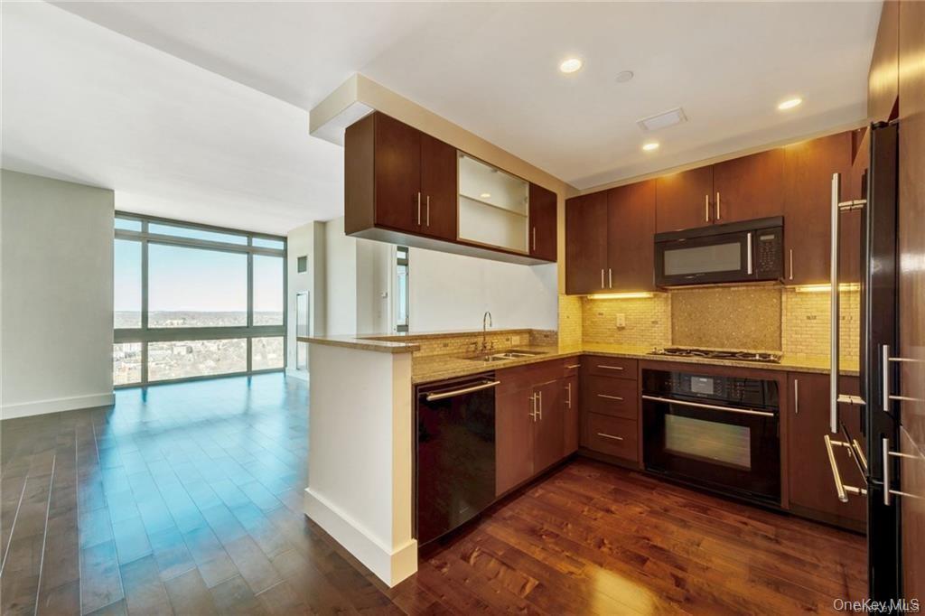 175 Huguenot Street, Unit 2404 New Rochelle, NY 10801 - Photo 2 of 8 Kitchen featuring a wall of windows, decorative backsplash, black appliances, light stone counters, and dark wood-style flooring