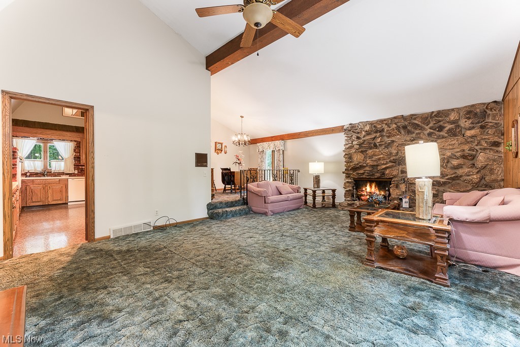19235 West Middletown Road Beloit, OH 44609 - Photo 13 of 35 Carpeted living room featuring a high ceiling, lofted ceiling with beams, ceiling fan with notable chandelier, and a fireplace