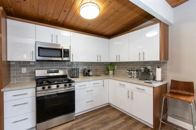 a kitchen with stainless steel appliances granite countertop a stove top oven a sink dishwasher and white cabinets with wooden floor