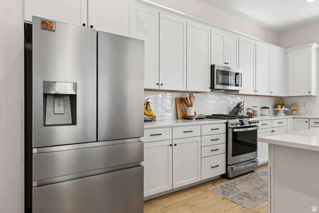 839 Walker Way St. George, UT 84770 - Photo 11 of 32 Contemporary kitchen featuring a stainless steel French door refrigerator, white shaker cabinetry with dark hardware, a stainless steel range with overhead microwave, white countertops, and a textured white tile backsplash