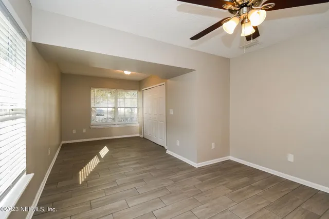 an empty room with wooden floor fan and windows