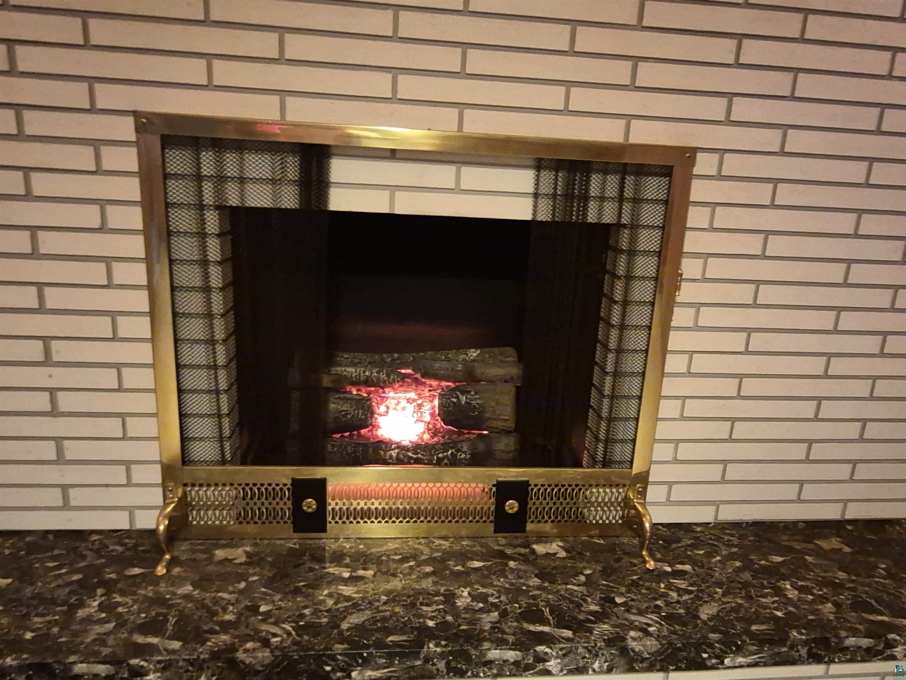 2109 West 22nd Street Duluth, MN 55811 - Photo 28 of 29 Fireplace featuring a brass-tone screen, faux log insert, and a surrounding white brick facade
