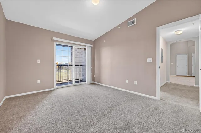 a view of an empty room with window and kitchen