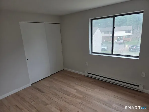 a view of an empty room with wooden floor and a window