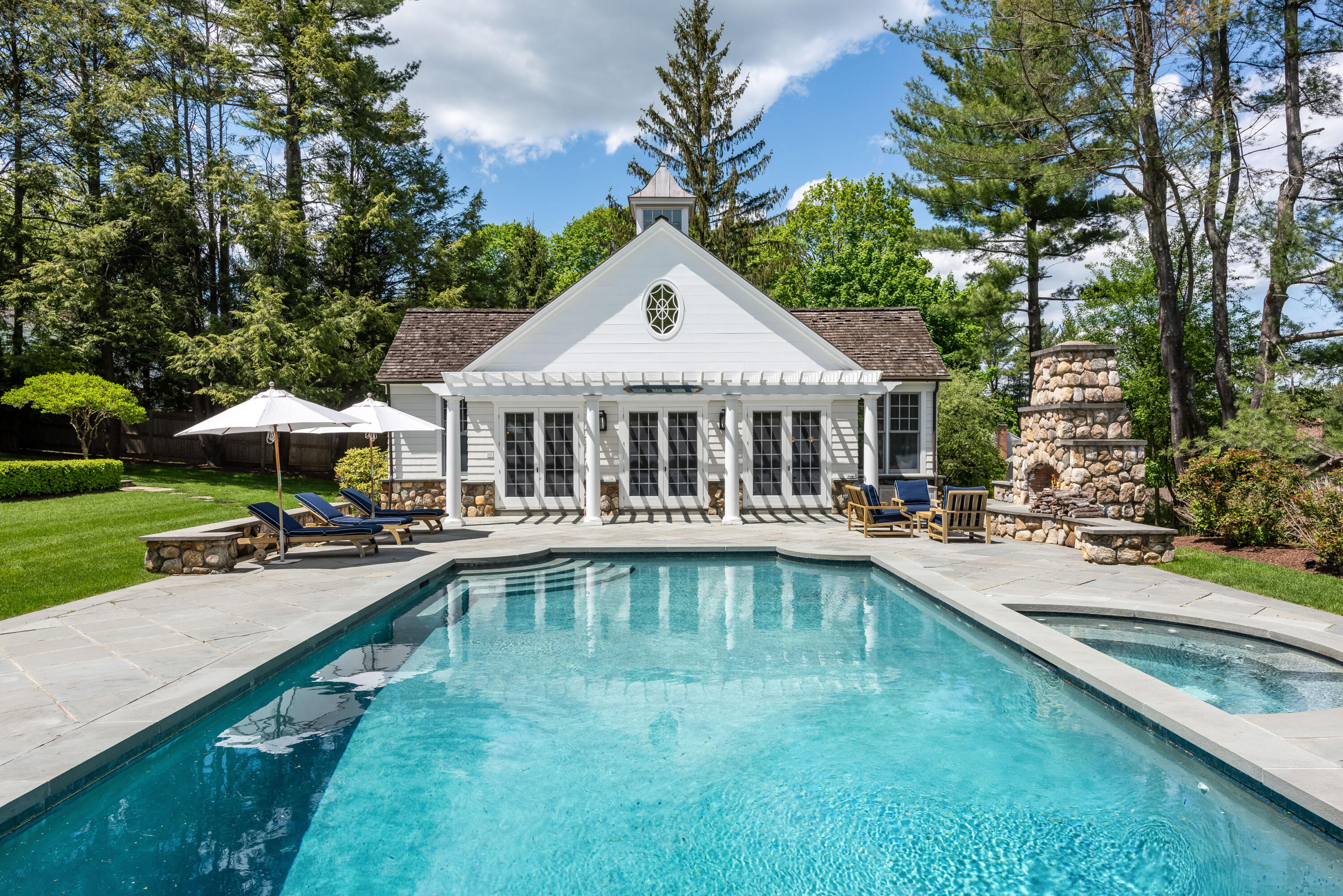 289 Oenoke Ridge New Canaan, CT 06840 - Photo 28 of 39 a white house with a large pool and lawn chairs under an umbrella