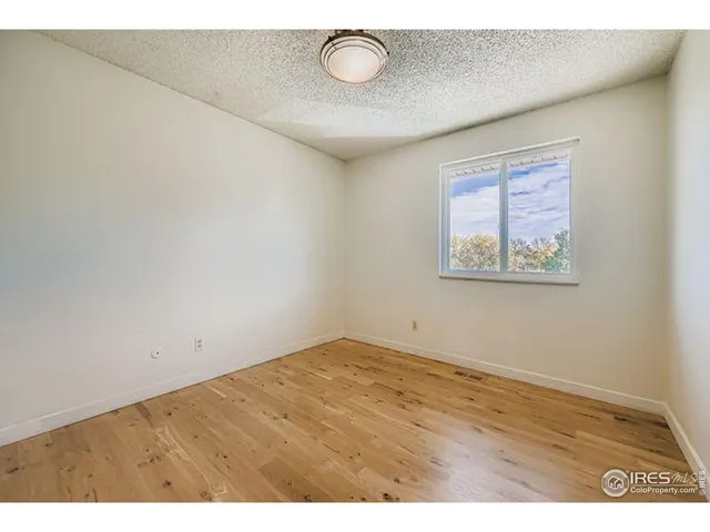 a view of an empty room with wooden floor and fan