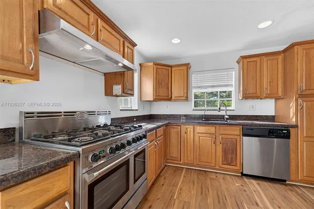 a kitchen with stainless steel appliances granite countertop a stove a sink dishwasher and a microwave oven with wooden floor