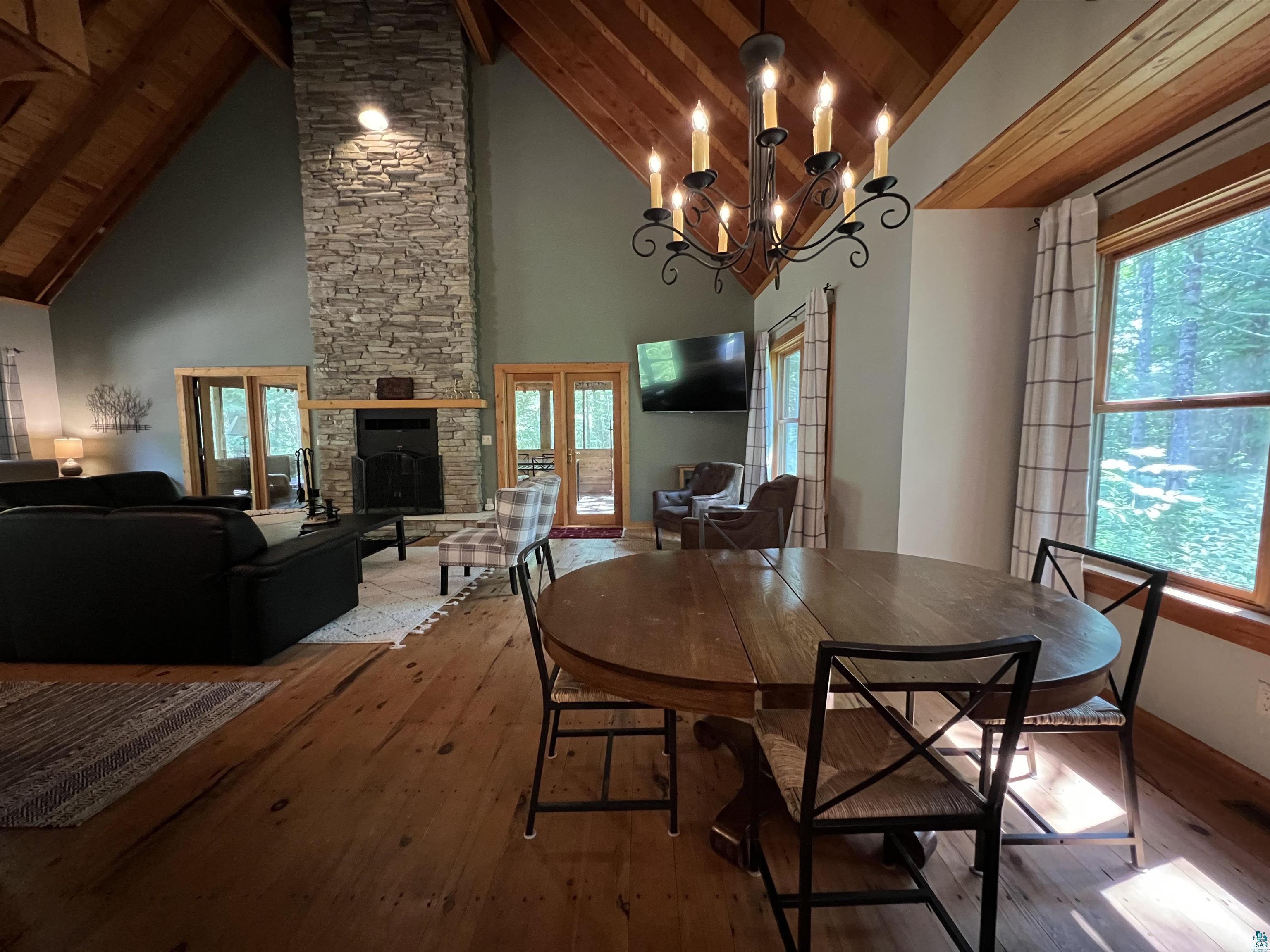 87645 Bjorn Road Bayfield, WI 54814 - Photo 2 of 13 Dining room featuring wood-type flooring, a stone fireplace, hanging lights, and a high wood beamed ceiling