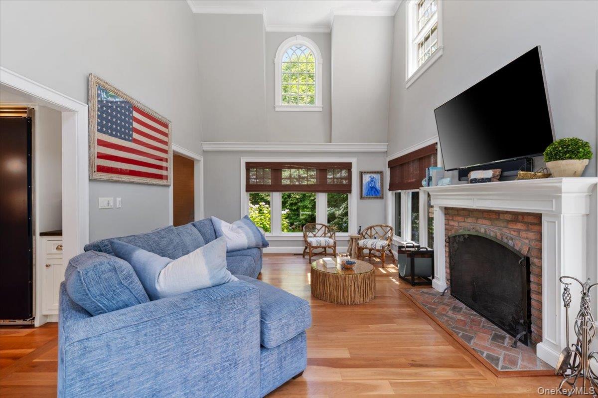 5 Fox Hunt Court Cold Spring Harbor, NY 11724 - Photo 7 of 42 Living area featuring hardwood flooring, a brick fireplace with a white mantel, and high ceilings