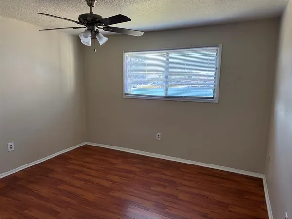 a view of a small space with wooden floor a ceiling fan and windows
