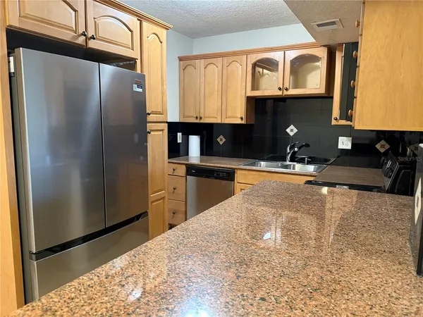 a kitchen with stainless steel appliances granite countertop a refrigerator a stove and a sink with wooden cabinets