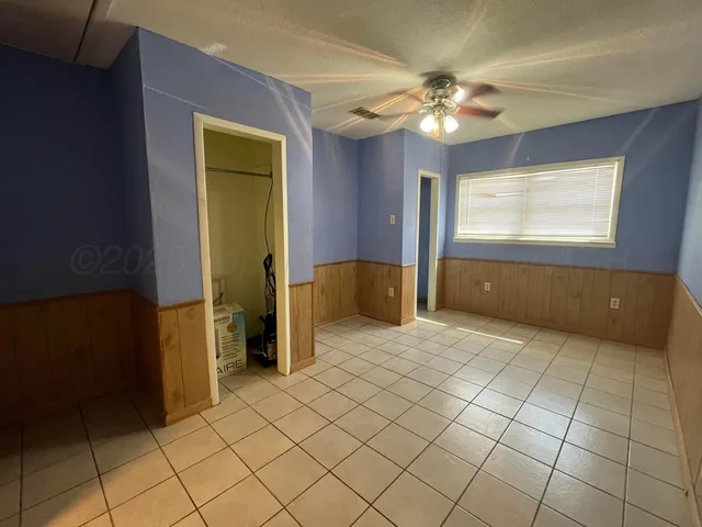 a view of an empty room with window and chandelier fan