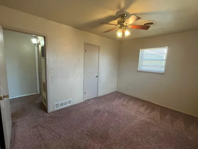 an empty room with a chandelier fan and windows