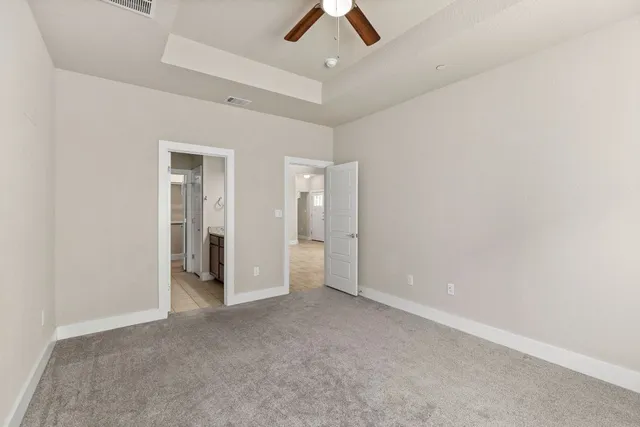 an empty room with chandelier fan and kitchen view