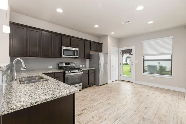 a kitchen with granite countertop stainless steel appliances a sink dishwasher a refrigerator cabinets and a window