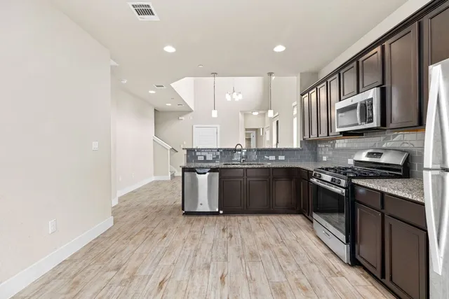 a large kitchen with stainless steel appliances granite countertop a stove a sink dishwasher and a microwave oven with wooden floor