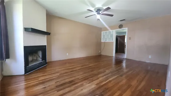 a view of an empty room with wooden floor and a fireplace