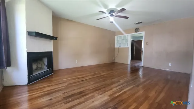 a view of an empty room with wooden floor and a fireplace