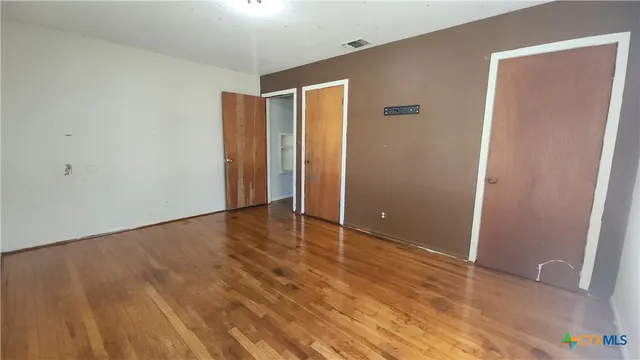 a view of an empty room with wooden floor and closet