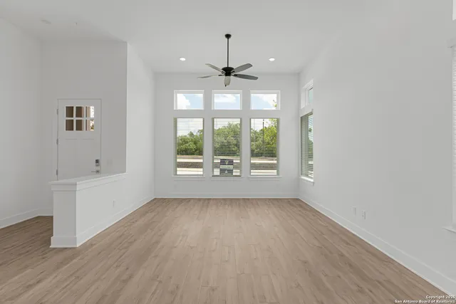 an empty room with wooden floor chandelier fan and windows