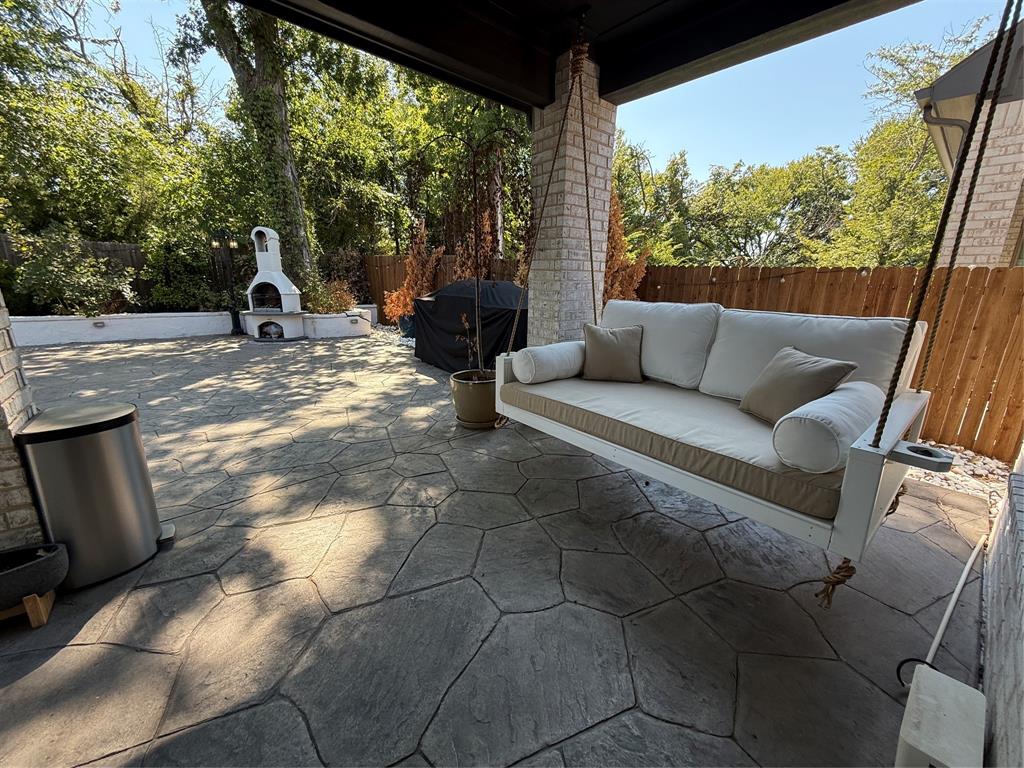 5212 Troupe Road McKinney, TX 75071 - Photo 33 of 38 Covered outdoor patio featuring a hanging daybed swing, flagstone-patterned concrete flooring, and a built-in outdoor fireplace