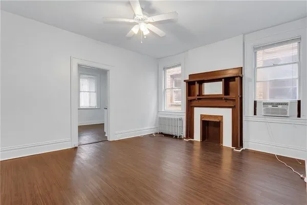 an empty room with wooden floor a ceiling fan a fireplace and windows
