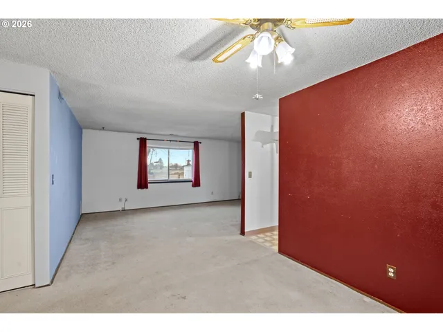 a view of an empty room with window and chandelier fan