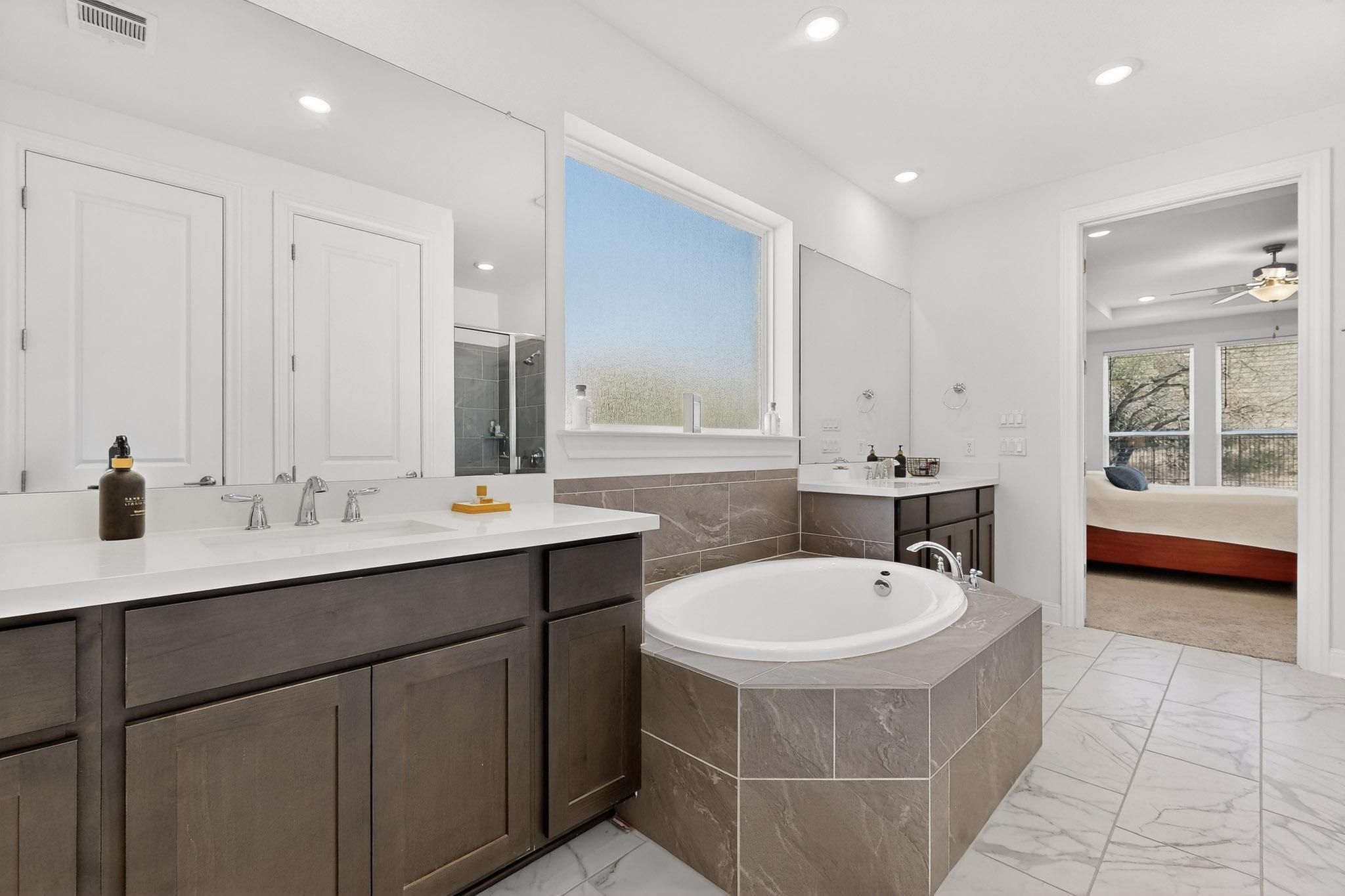 249 Running Bird Road Austin, TX 78737 - Photo 17 of 40 Ensuite Primary bathroom with two vanities, a shower stall, light marble finish floors, a garden tub, and recessed lighting