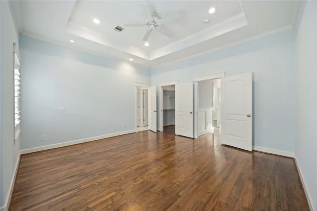 an empty room with wooden floor ceiling fan and windows