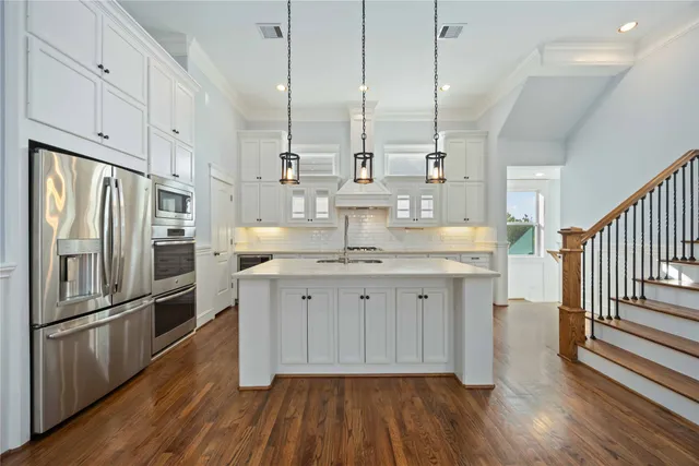 a kitchen with stainless steel appliances granite countertop a refrigerator a oven and white cabinets with wooden floors