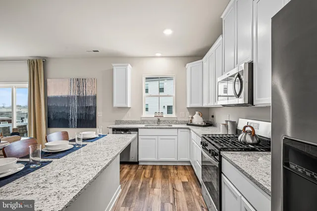 a open kitchen with stainless steel appliances granite countertop a stove top oven a sink dishwasher a dining table and chairs with wooden floor