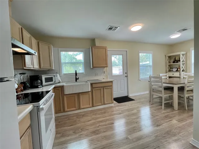 a kitchen with stainless steel appliances granite countertop a stove top oven a sink a dining table and chairs with wooden floor