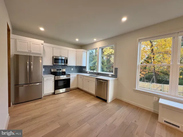 a kitchen with stainless steel appliances a refrigerator a sink wooden floor and a large window