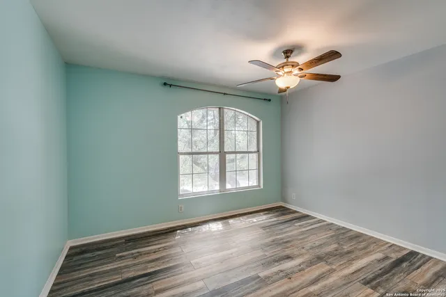 an empty room with wooden floor fan and windows
