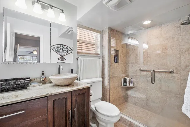 a bathroom with a granite countertop sink a toilet a mirror a vanity and shower