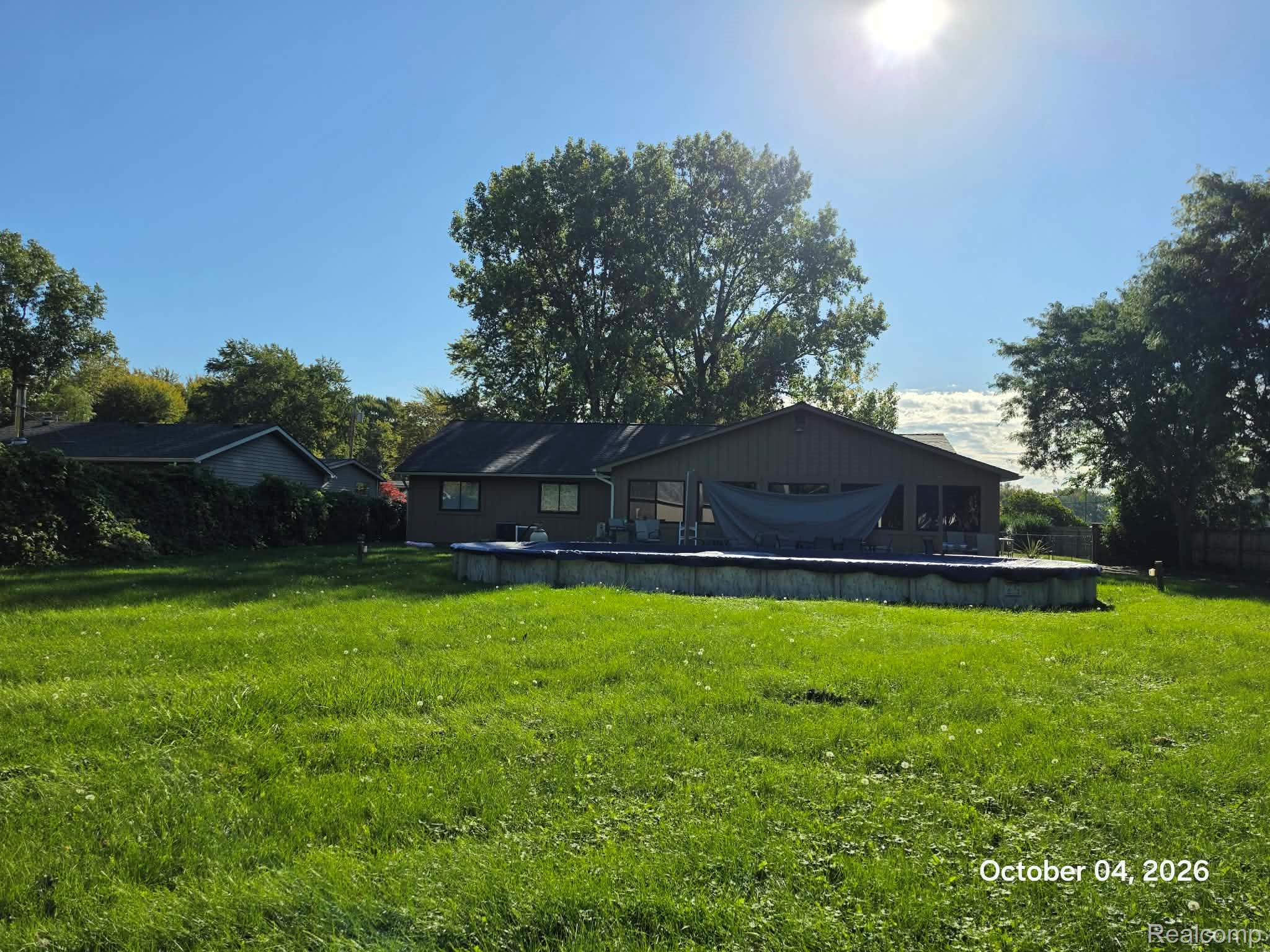34781 Union Lake Road Clinton Township, MI 48035 - Photo 35 of 38 Expansive grassy area featuring a covered above-ground pool, a rear patio with screened sections, and mature perimeter trees