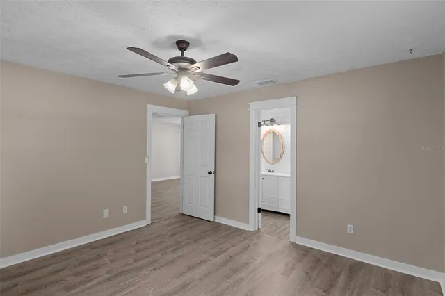 a view of an empty room with wooden floor and a ceiling fan