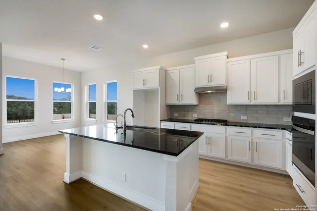 a kitchen with stainless steel appliances a stove a sink a refrigerator white cabinets and wooden floor