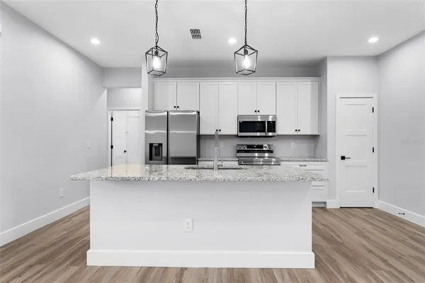 a kitchen with stainless steel appliances granite countertop a sink a refrigerator a stove a microwave and white cabinets with wooden floor