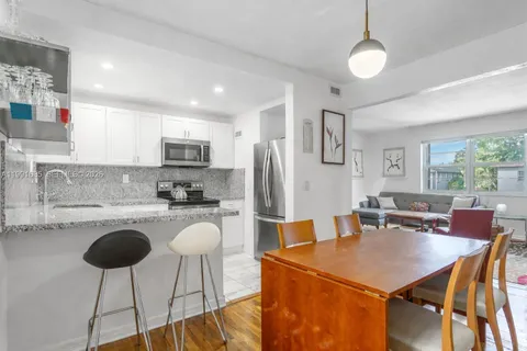 a open kitchen with stainless steel appliances granite countertop a dining table chairs refrigerator and sink