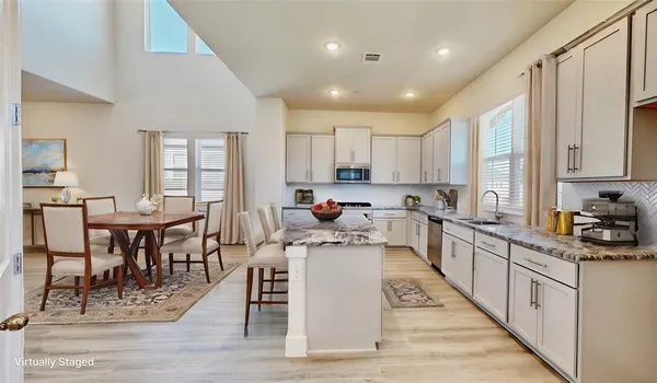 a kitchen with stainless steel appliances granite countertop a stove top oven a sink dishwasher a dining table and chairs with wooden floor