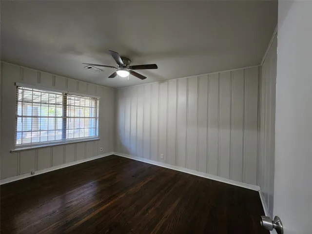 an empty room with wooden floor fan and windows