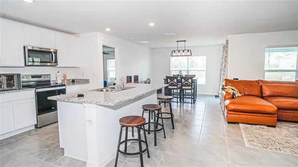 a kitchen with stainless steel appliances kitchen island granite countertop a refrigerator a stove a dining table and chairs