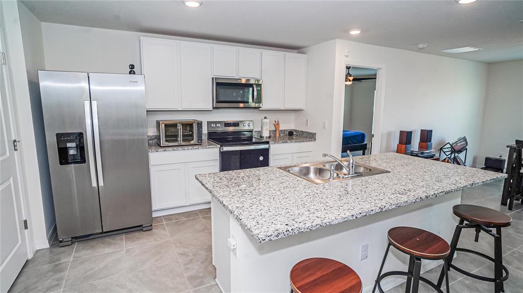 13253 Mylion Way Spring Hill, FL 34610 - Photo 5 of 31 a kitchen with stainless steel appliances granite countertop a kitchen island a stove a refrigerator a sink a dining table and chairs