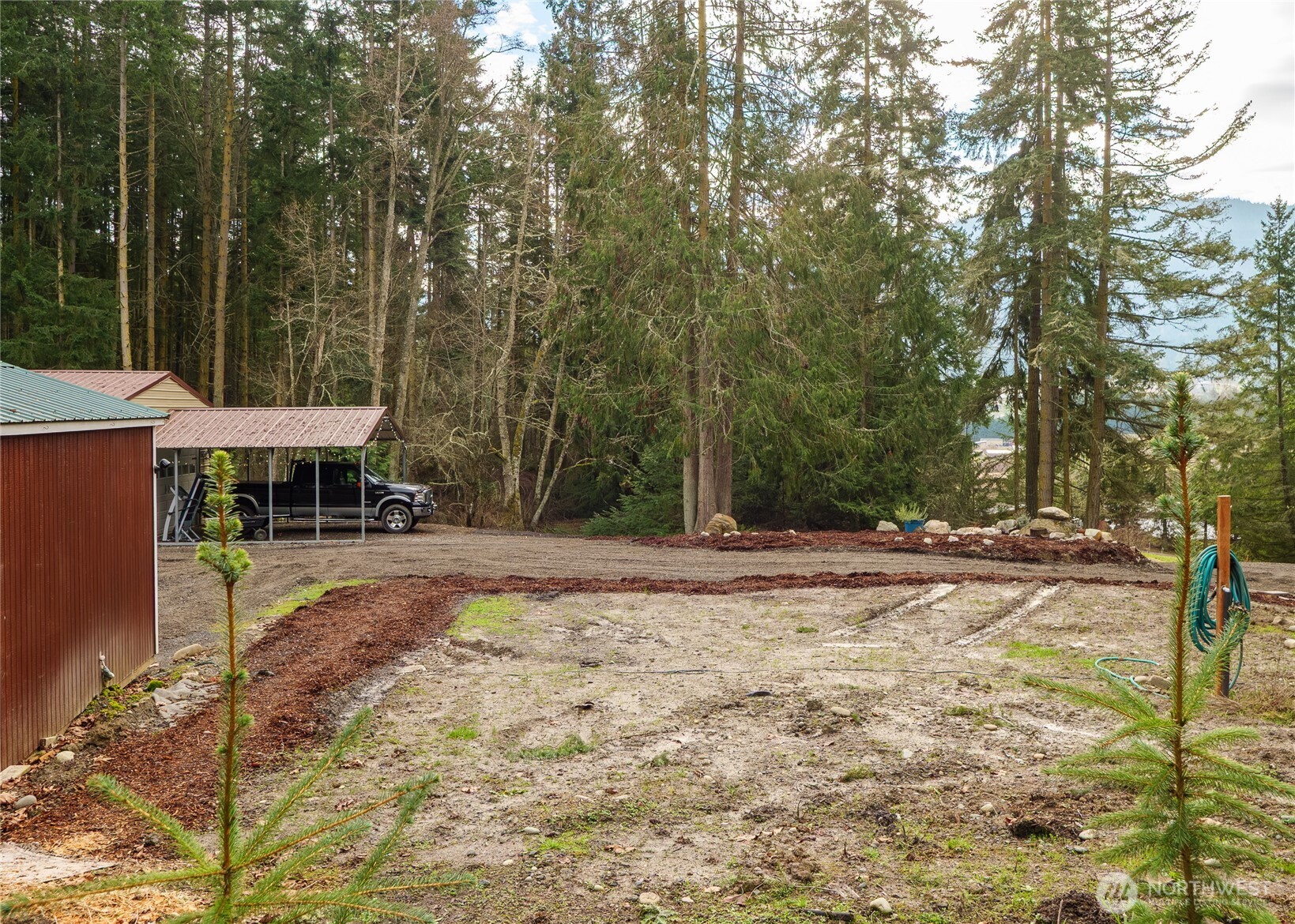 193 Springwater Lane Sequim, WA 98382 - Photo 17 of 40 a view of a backyard with table and chairs a barbeque with potted plants and large trees