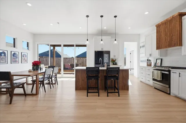 a kitchen with stainless steel appliances granite countertop a stove top oven a sink a dining table and chairs with wooden floor