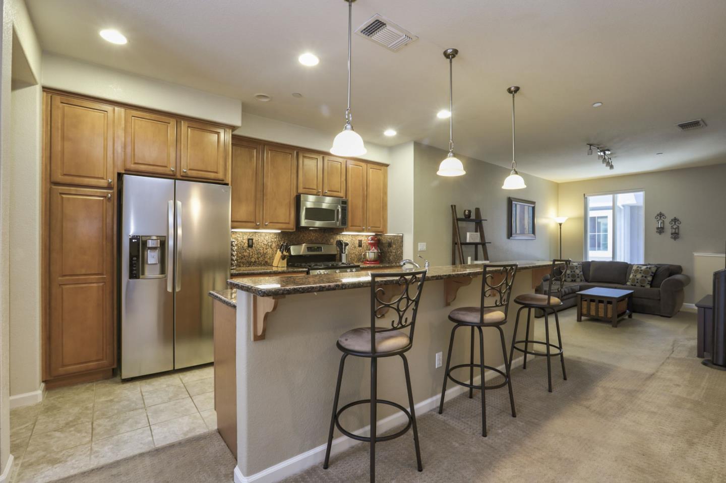 a kitchen with stainless steel appliances kitchen island granite countertop a refrigerator a stove a sink a dining table and chairs with wooden floor