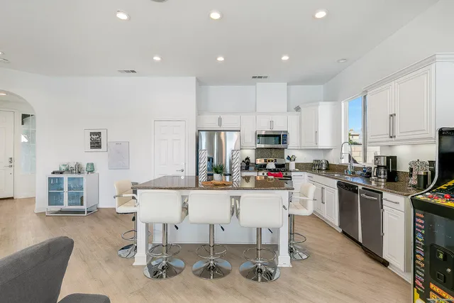 a kitchen with stainless steel appliances kitchen island granite countertop a stove a refrigerator a kitchen island and chairs with wooden floor