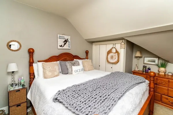a bedroom with a bed and a lamp on dresser next to a window