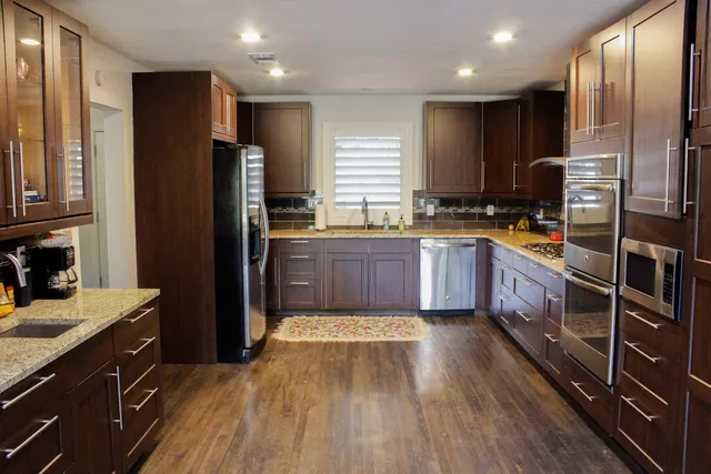 a kitchen with stainless steel appliances granite countertop a refrigerator a stove a sink dishwasher and wooden cabinets with wooden floor